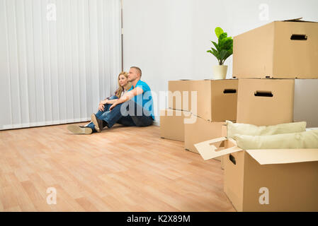 Junges Paar sitzt auf Parkett im neuen Haus mit Stapel von Kisten Stockfoto