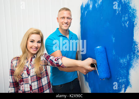 Portrait von glückliches junges Paar Malerei Wand mit Farbroller Stockfoto