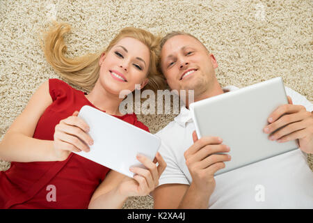 Glückliches Paar Liegen auf dem Teppich halten Digitale Tabletten Stockfoto