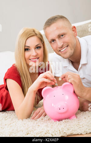 Portrait von glückliches junges Paar einfügen Münze in Sparschwein Stockfoto