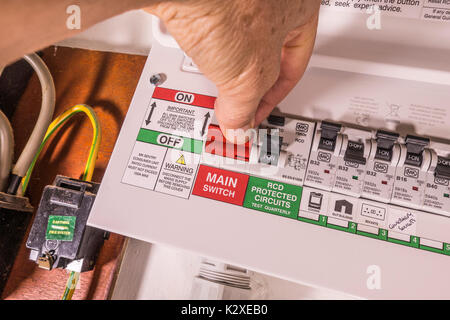 Der Mann Daumen und Finger auf der Haupt-EIN/AUS-Schalter der Eine neu montierte Strom Verbraucher, mit mehreren Switches. England, UK. Stockfoto