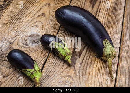 Ein großer und zwei kleine Aubergine auf Holz- Hintergrund. Studio Foto Stockfoto