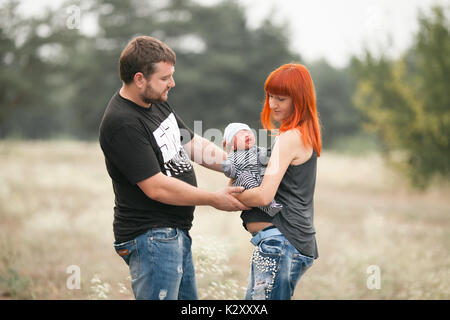 Glückliche junge Familie mit neugeborenen Babys auf Spaziergang im Park. Mutter hält in ihren Händen schreien neugeborenes Baby, Vater nahe steht. Stockfoto