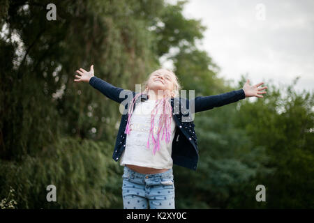 Kind, Mädchen, Lächeln, fühlt sich glücklich, die Freude und die Freude am Laufen. Sie öffnete ihre Hände auf die Seite und schloss die Augen. Stockfoto