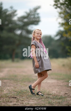 Glückliches Kind Mädchen mit Zöpfen steht auf einem Spaziergang im Park. Stockfoto