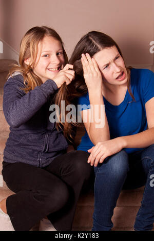 Schwestern setzte sich auf die Treppe zu Hause mit einem ziehen die anderen Haare. Stockfoto