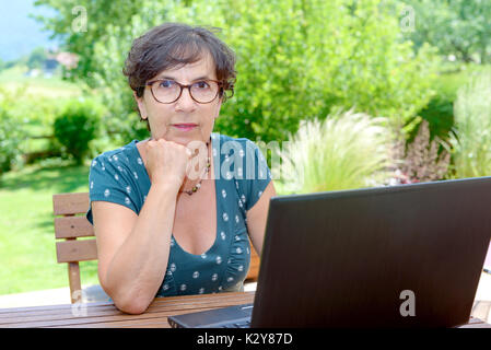 Modern casual reife Frau sitzt auf der Terrasse Garten mit Laptop Stockfoto