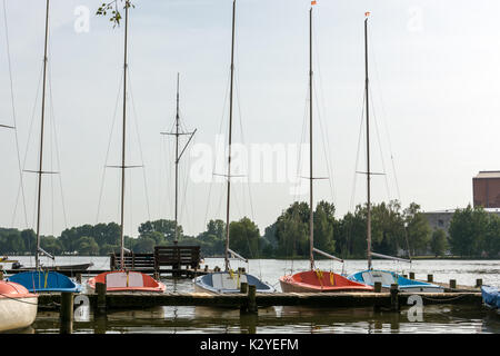 Mehrere Segelboote an einer hölzernen Pier an einem See. Stockfoto