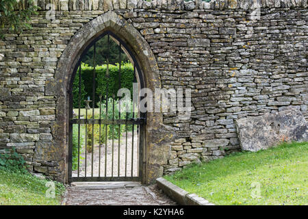 Gewölbte gated Eingang und einer Steinmauer auf dem Gelände des St. Andrew's Kirchhof, Chedworth, Cotswolds, Gloucestershire, England Stockfoto