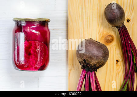 Glas Glas mit eingemachten Rüben hausgemacht und frisch Bio rote Rüben mit Haulm mit Schneidbrett aus Holz auf einem weißen Hintergrund, Ansicht von oben Stockfoto