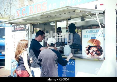 Eine Frau und zwei Männer stehen zusammen bestellen, von einer 'NC-Rippen" essen Fahrzeug während der Spring Fair, einer studentischen Spring Carnival an der Johns Hopkins University, Baltimore, Maryland, April, 2016. Mit freundlicher Genehmigung von Eric Chen. Stockfoto