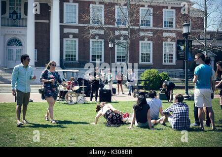 Die Schüler gehen mit Getränken und sitzen auf dem Gras ein Student Band spielen vor Gilman Hall zu genießen, während der Spring Fair, ein Kursteilnehmer - Spring Carnival an der Johns Hopkins University, Baltimore, Maryland, April, 2016. Mit freundlicher Genehmigung von Eric Chen. Stockfoto