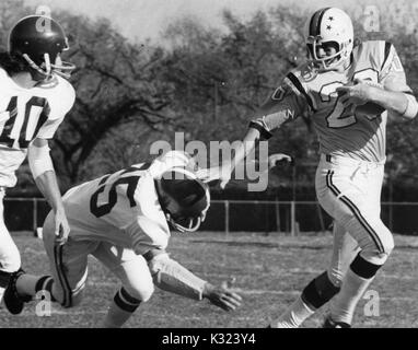 Ein Johns Hopkins University football player ausgeführt mit der Fußball und das Halten der gegnerischen Mannschaft Spieler, fällt mit der Hand auf dem Feld an der Johns Hopkins University, Baltimore, Maryland, 1975. Stockfoto