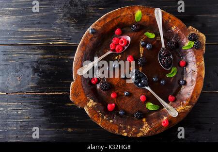 Frische reife Beeren Himbeeren Brombeeren und Heidelbeeren auf braunem Holz- Platte mit einem Löffel auf einer schwarzen Holztisch, rustikal, selektiver Fokus, Spa Stockfoto