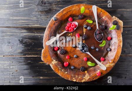 Frische reife Beeren Himbeeren Brombeeren und Heidelbeeren auf braunem Holz- Platte mit einem Löffel auf einer schwarzen Holztisch, rustikal, selektiver Fokus, Spa Stockfoto