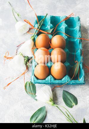 Rohe Eier im Karton für Eier mit weißen Blumen auf einem Marmor weißer Tisch, für die Lackierung von Ostern, der Raum unter dem Text, selektiven Fokus bereit Stockfoto