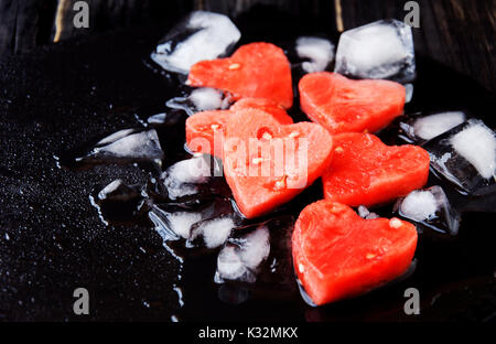 Wassermelone Herzen mit Eiswürfel auf schwarzen Stein Hintergrund für Valentinstag, selektiver Fokus, Platz für Text Stockfoto