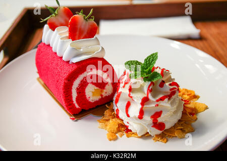 Erdbeere auf Red Velvet Cake roll mit Schlagsahne und Getreide auf weiße Schale. Stockfoto