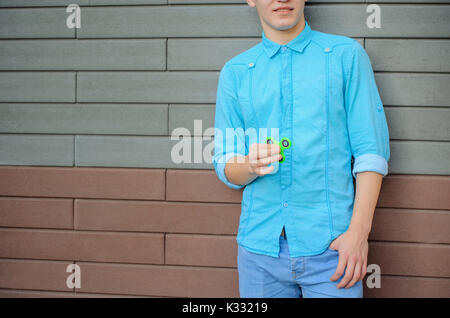 In der Nähe eines beliebten zappeln grüne Spinner in der Hand eines Jugendlichen. Der Kerl spielt eine schlafende Spinner auf der Mauer Hintergrund. Stockfoto