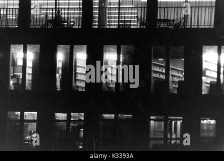 In der Nacht, die Ebenen innerhalb des Milton S Eisenhower Bibliothek leuchten die Fenster, die Stapel von Büchern und die Silhouetten von Studenten, die an Tischen und an Stühlen, von einer Stufe zu Stufe B und M-Ebene an der Spitze, der Johns Hopkins University, Baltimore, Maryland, 1965. Stockfoto