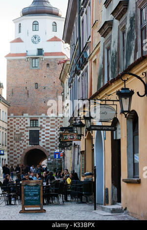 Diners an Tischen im Freien in der Altstadt von Lublin entfernt. Krakauer Tor ist im Hintergrund. Stockfoto