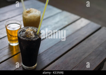Eis schwarzen Kaffee in hohen Glas auf Holztisch, Hintergrund, Thai Vintage Style Trinken. seichte konzentrieren. Stockfoto