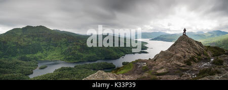 Ein Mann stand auf dem Gipfel des Ben A'an in den schottischen Highlands, Schottland. Vor der atemberaubenden Vista/view mit Wolken Hervorhebung der Abenteurer. Stockfoto