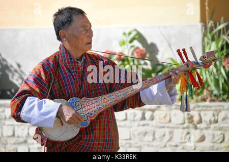 PARO, BHUTAN - November 10, 2012: Unbekannter alter Mann Musiker in traditioneller Kleidung (GHO) spielen Dramnyen Instrument im Hotel in Paro, Bhutan Stockfoto