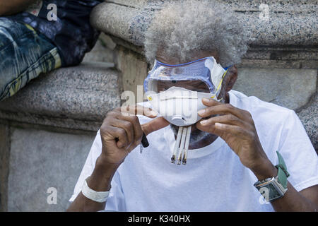 Ein Mann, der drei Zigaretten gleichzeitig raucht, während er eine Schutzbrille und eine Gesichtsmaske trägt, in Lower Manhattan, New York City Stockfoto