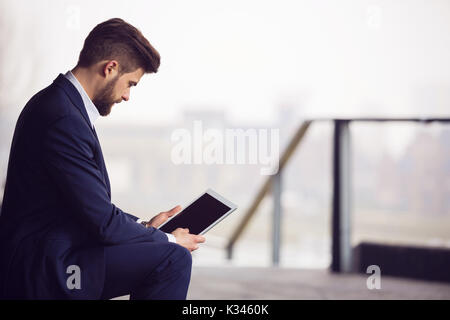Ein Foto der jungen, gut aussehenden Geschäftsmann außerhalb und über Tablet-PC sitzen. Stockfoto