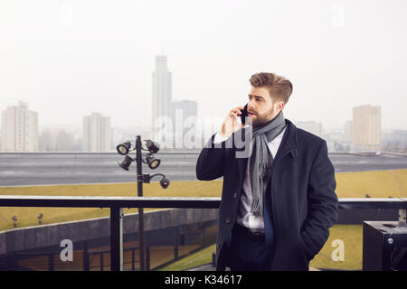 Ein Foto der jungen, gutaussehenden Mann irgendwo außerhalb der städtischen Hintergrund stehen. Er spricht auf das Handy. Stockfoto