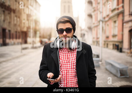 Ein Foto der jungen, trendigen Mann stand auf dem Stadtplatz und Simsen. Stockfoto