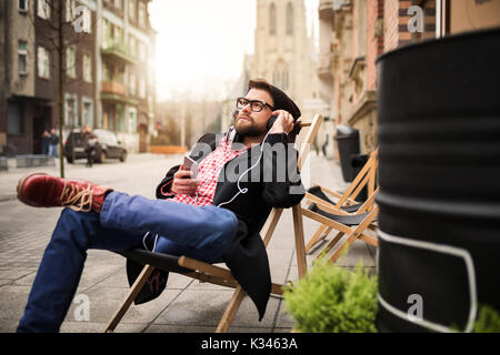 Ein Foto des jungen Mannes entspannen auf dem Liegestuhl und hören Musik. Stockfoto