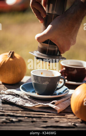 Mann filter Kaffee brühen Outdoor, im Herbst Kaffee Picknick, auf dem alten beschädigt Holztisch Hintergrund. Kaffee tropft in Bewegung in der Pro erfasst Stockfoto