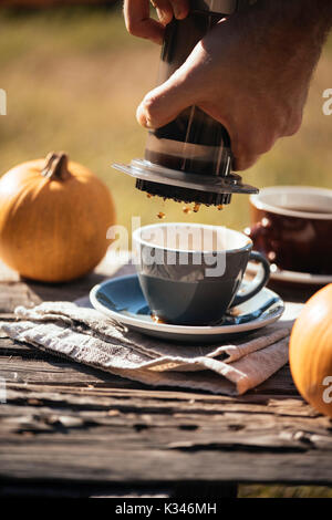 Mann filter Kaffee brühen Outdoor, im Herbst Kaffee Picknick, auf dem alten beschädigt Holztisch Hintergrund. Kaffee tropft in Bewegung in der Pro erfasst Stockfoto