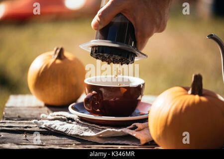 Mann filter Kaffee brühen Outdoor, im Herbst Kaffee Picknick, auf dem alten beschädigt Holztisch Hintergrund. Kaffee tropft in Bewegung in der Pro erfasst Stockfoto