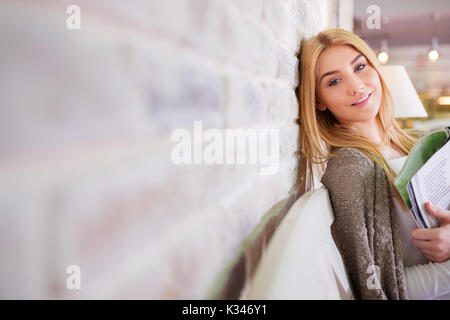 Ein Foto der jungen, schönen Frau glücklich lächelnd in die Kamera. Sie ist eine Zeitschrift und lehnte sich gegen die Wand. Stockfoto