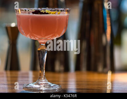 Rosa cocktail garniert mit Blumen in Margarita Glas. Alkoholische Getränk in hohes Glas auf die Theke der Bar aus Holz Stockfoto
