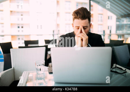 Business mann Woking am Laptop mit Kopfschmerzen im Café auf der Terrasse. Stockfoto