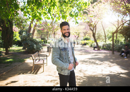 Ein Foto der jungen, gutaussehenden Mann stand auf der Allee im Park. Er ist glücklich lächelnd. Stockfoto