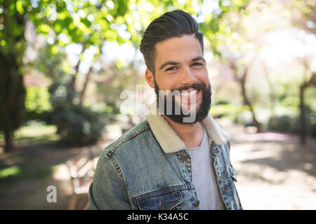 Ein Foto der jungen, gut aussehenden Mann zu dem Foto posiert und glücklich lächelnd. Er steht auf der Allee im Park. Stockfoto