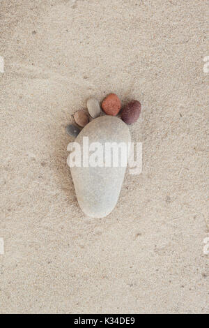Gruppe von Kieselsteinen auf Sand de Form eines Fußes in isolierten weißen Hintergrund. Stockfoto