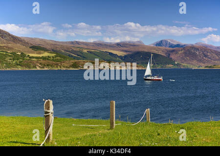 Segelyacht am Meer mit Gebirge im Hintergrund und grüne Wiese des Meeres im Vordergrund, Ullapool, Wester Ross, Schottland Stockfoto