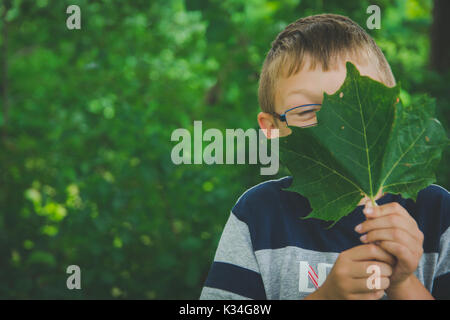 Ein kleiner Junge hält ein grünes Blatt vor seinem Gesicht. Stockfoto