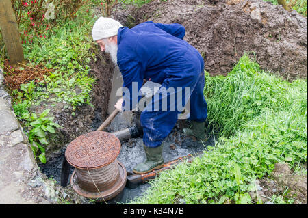 Klempner gräbt ein Loch, um verstopfte Abflüsse in Irland zu reparieren. Stockfoto