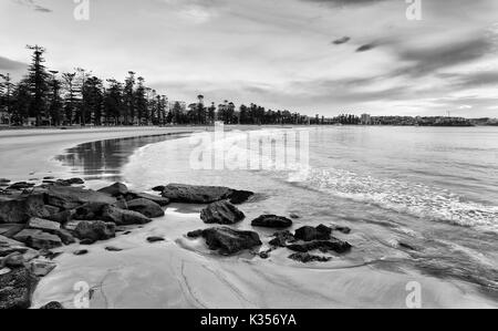 Flache Ufer von sandy Manly Beach in Sydney Northern Beaches mit glatten verschwommen Welle langsam Rollen zu küstennahen Felsen bei Ebbe. Stockfoto