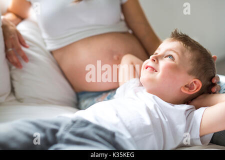 Eine schöne schwangere junge Mutter, im Bett sitzen mit ihrem älteren Kind Stockfoto