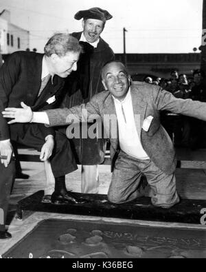 Al Jolson feiert gerade seine Hand, Fuß und Knie - druckt im Beton von Sid Grauman Chinese Theatre in Hollywood. Sid Grauman ist links direkt auf Jolson. Stockfoto