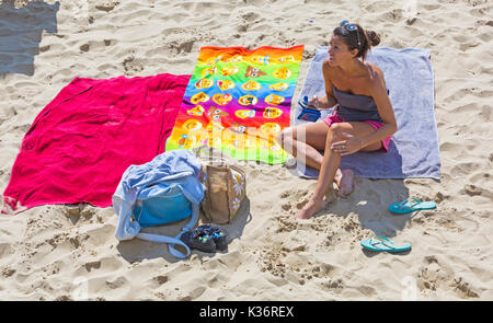 Bournemouth, Dorset, Großbritannien. Sept. 2017. Wetter in Großbritannien: Schöner, sonniger Tag am Strand von Bournemouth. Frau entspannt in der Sonne auf dem Handtuch sitzend, das Handy iPhone Smartphone Handy hält. Credit: Carolyn Jenkins/Alamy Live News Stockfoto