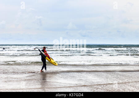 Eine einzelne männliche Surfer seine gelben und schwarzen Surf Board auf das Meer bei Westward Ho!, Devon, England, Großbritannien Stockfoto